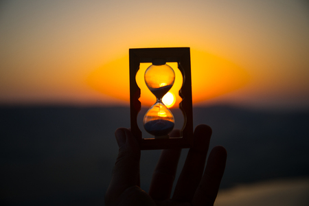 Life time passing concept. Hand holding hourglass with sunset sky background. Selective focus