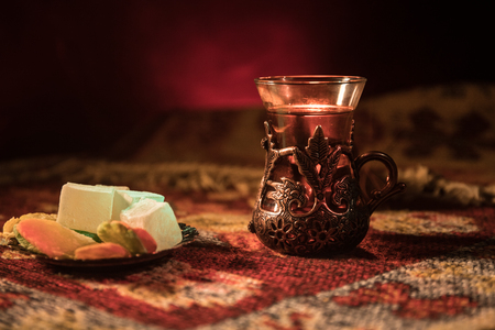 Arabian tea in glass with eastern snacks on a carpet on dark background with lights and smoke. Eastern tea concept. Empty space. Selective focus.の写真素材