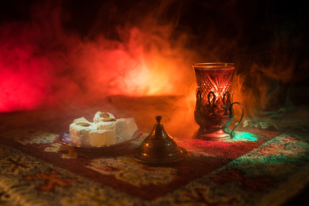 Arabian tea in glass with eastern snacks on a carpet on dark background with lights and smoke. Eastern tea concept. Empty space. Selective focus.の写真素材