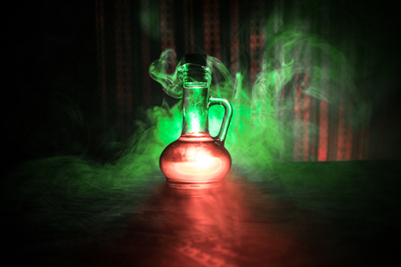 Antique and vintage glass bottle on dark foggy background with light. Poison or magic liquid concept.の写真素材