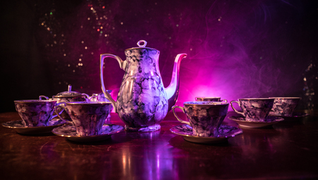 Coffee or tea ceremony conceptual theme. Old vintage ceramic tea or coffee pot with cups jug and sugar cup on dark toned background with light and smoke. Empty space for text. Selective focusの写真素材