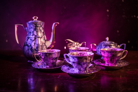 Coffee or tea ceremony conceptual theme. Old vintage ceramic tea or coffee pot with cups jug and sugar cup on dark toned background with light and smoke. Empty space for text. Selective focusの写真素材