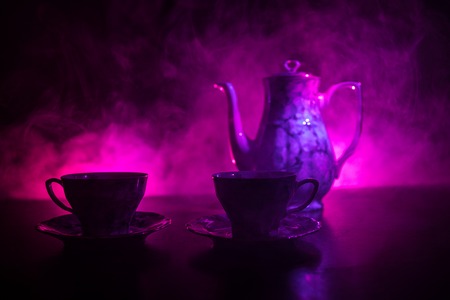 Coffee or tea ceremony conceptual theme. Old vintage ceramic tea or coffee pot with cups on dark...