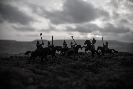 Medieval battle scene with cavalry and infantry. Silhouettes of figures as separate objects, fight between warriors on sunset foggy background. Selective focusの写真素材