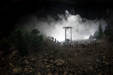 Silhouette of a large crowd of people in forest at night standing against a big hourglass with toned...