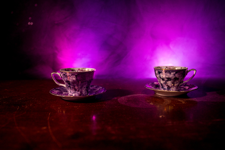 Coffee or tea ceremony conceptual theme. Old vintage ceramic tea or coffee cups on dark toned background with light and smoke. Empty space for text. Selective focusの写真素材