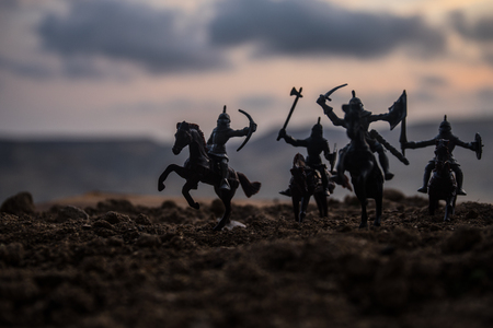 Medieval battle scene with cavalry and infantry. Silhouettes of figures as separate objects, fight between warriors on sunset foggy background. Selective focusの写真素材