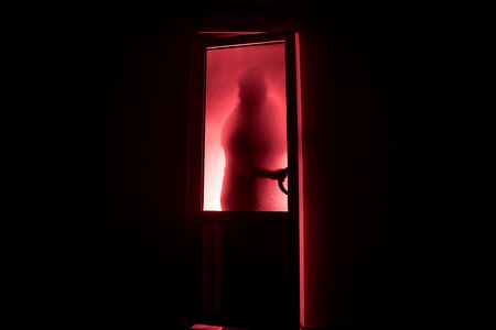 Silhouette of an unknown shadow figure on a door through a closed glass door. The silhouette of a human in front of a window at night. Scary scene halloween concept of blurred silhouette of maniac.の写真素材