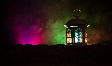 Ornamental Arabic lantern with burning candle glowing at night on dark toned foggy background. Festive greeting card, invitation for Muslim holy month Ramadan Kareem(Eid Holiday) Dark background.の写真素材