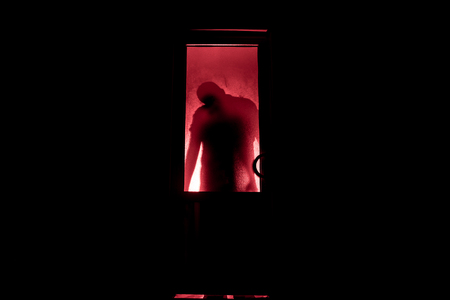 Silhouette of an unknown shadow figure on a door through a closed glass door. The silhouette of a human in front of a window at night. Scary scene halloween concept of blurred silhouette of maniac.の写真素材