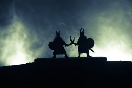 Silhouette of two medieval warriors in duel. Picture with two fighter with sword with dark toned foggy background. Selective focus.の写真素材