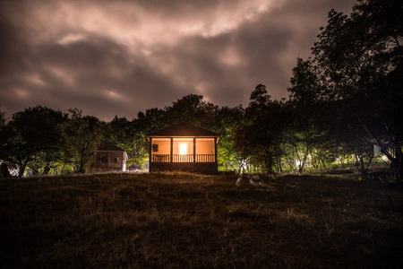 Mountain night landscape of building at forest at night with moon or vintage country house at night with clouds and stars. Summer night. Photo taken with long exposureの写真素材