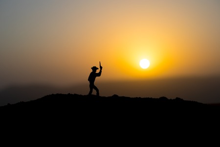 Cowboy concept. Silhouette of Cowboy at sunset time. A cowboy silhouette on a mountain with an yellow sky. Selective focusの写真素材
