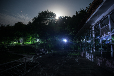 Mountain night landscape of building at forest at night with moon or vintage country house at night with clouds and stars. Summer night. Photo taken with long exposureの写真素材