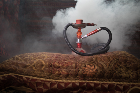 Hookah hot coals on shisha bowl making clouds of steam at Arabian interior. Oriental ornament on the...