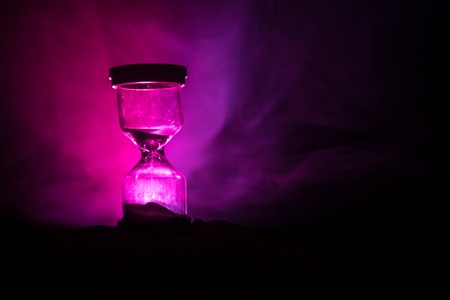 Time concept. Silhouette of Hourglass clock and smoke on dark background with hot yellow orange red...