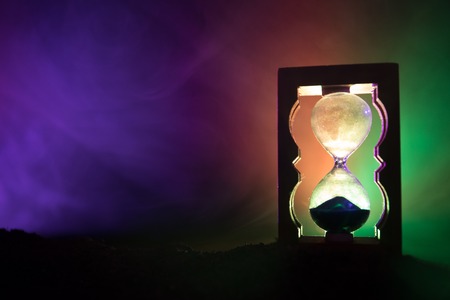Time concept. Silhouette of Hourglass clock and smoke on dark background with hot yellow orange red...