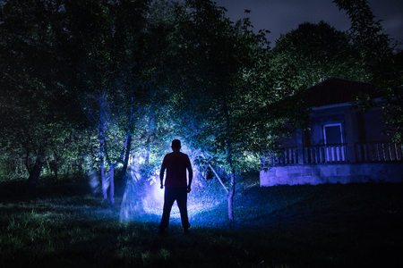 Silhouette of man in the forest on the night. Silhouette of person standing in the dark forest with light. Dark night in forest. Surreal night forest scene. Horror Halloween concept.の写真素材