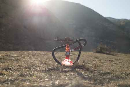 Hookah, traditional arabic waterpipe, direct sunset light, outdoor photo. Mountain background....