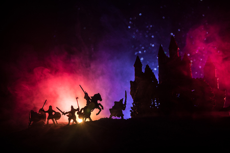 Medieval battle scene with cavalry and infantry. Silhouettes of figures as separate objects, fight between warriors on dark toned foggy background with medieval castle. Selective focusの写真素材