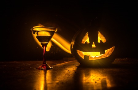Halloween pumpkin orange cocktails. Festive drink. Halloween party. Funny Pumpkin with a glowing cocktail glass on a dark toned foggy background. Selective focusの写真素材