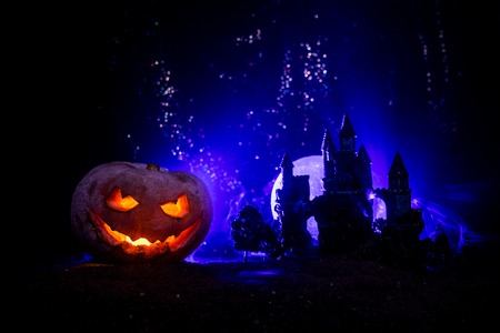 Horror view of Halloween pumpkin with scary smiling face. Head jack lantern with haunted building and tree on dark toned foggy background.の写真素材