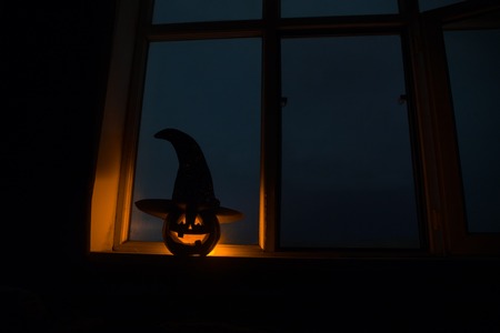 Scary Halloween pumpkin in the mystical house window at night or halloween pumpkin in night on room with blue window. Symbol of halloween in window. Selective focusの写真素材