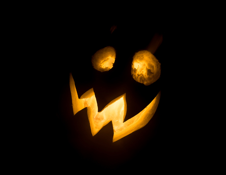 Halloween pumpkin smile and scrary eyes for party night. Close up view of scary Halloween pumpkin with eyes glowing inside at black background. Selective focusの写真素材