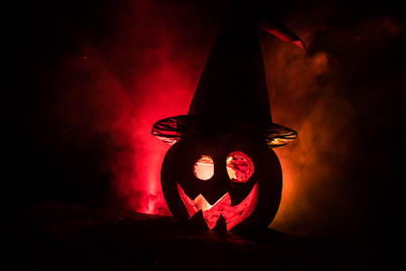 Halloween concept. Jack-o-lantern smile and scary eyes for party night. Close up view of scary pumpkin with witch hat on at dark foggy background. Selective focus. Empty spaceの写真素材