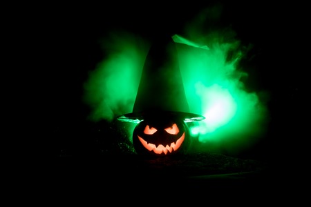 Halloween concept. Jack-o-lantern smile and scary eyes for party night. Close up view of scary pumpkin with witch hat on at dark foggy background. Selective focus. Empty spaceの写真素材