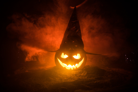Halloween concept. Jack-o-lantern smile and scary eyes for party night. Close up view of scary pumpkin with witch hat on at dark foggy background. Selective focus. Empty spaceの写真素材