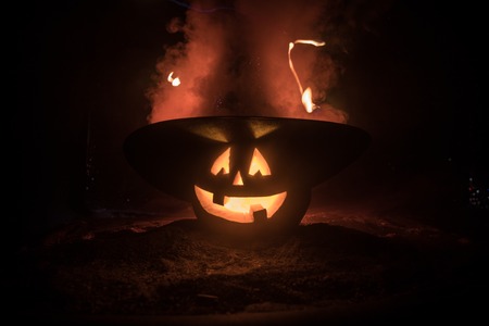 Halloween concept. Jack-o-lantern smile and scary eyes for party night. Close up view of scary pumpkin with witch hat on at dark foggy background. Selective focus. Empty spaceの写真素材