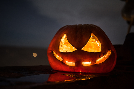 Horror Halloween concept. Close up view of scary dead Halloween pumpkin glowing at dark background. Rotten pumpkin head. Selective focusの写真素材