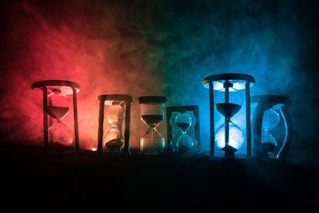 Time concept. Silhouettes of Hourglasses on dark toned foggy background with back lighting. Abstract surreal concept with copy space. Selective focusの写真素材