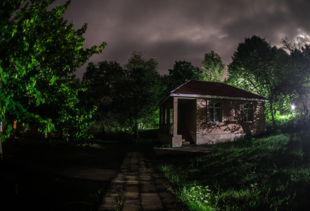 Mountain night landscape of building at forest at night with moon or vintage country house at night with clouds and stars. Summer night. Photo taken with long exposureの写真素材