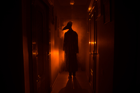 Creepy silhouette in the dark abandoned building. Horror Halloween concept. Dark corridor with silhouette of horror person standing in center. Toned light and fog on background.の写真素材