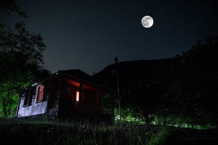 Mountain night landscape of building at forest at night with moon or vintage country house at night...
