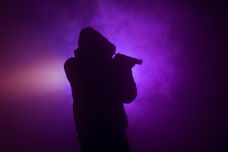 Silhouette of man with pistol ready to attack on dark toned foggy background or dangerous bandit holding gun in hand. Shooting terrorist with weapon theme decorの写真素材