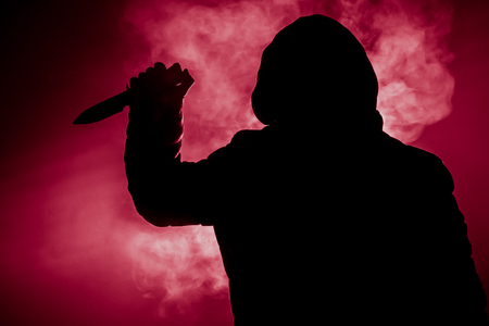A dangerous hooded man standing in the dark and holding a knife. Face can not be seen. Committing a crime conceptの写真素材