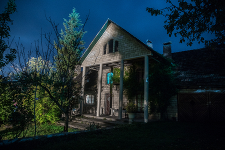 Mountain night landscape of building at forest at night with moon or vintage country house at night with clouds and stars. Summer night. Photo taken with long exposureの写真素材