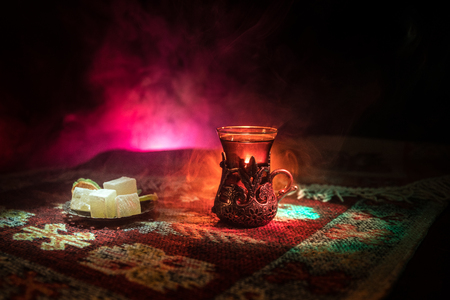 Arabian tea in glass with eastern snacks on a carpet on dark background with lights and smoke. Eastern tea concept. Empty space. Selective focus.の写真素材