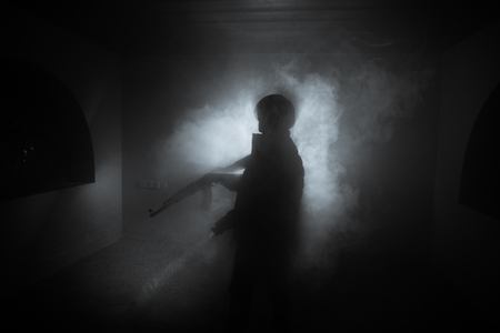 Silhouette of man with assault rifle ready to attack on dark toned foggy background or dangerous bandit holding gun in hand. Shooting terrorist with weapon theme decorの写真素材