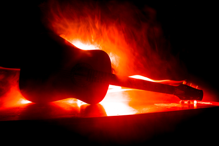 Music concept. Acoustic guitar on a dark background under beam of light with smoke with copy space. Exploding guitar. Fire effects. Surreal guitar. Selective focusの写真素材