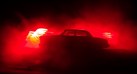Silhouette of old vintage car in dark foggy toned background with glowing lights in low light. Selective focusの写真素材