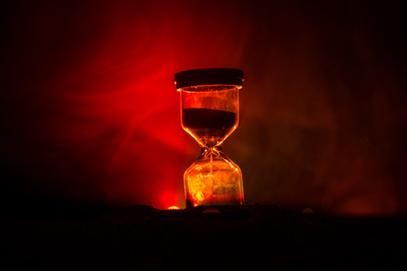 Time concept. Silhouette of Hourglass clock and smoke on dark background with hot yellow orange red blue cold back lighting, with copy space. Selective focusの写真素材