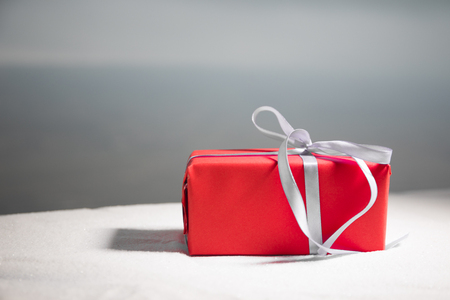Christmas or New Year gift with ribbon in snow on bokeh background. Copy space for text. Winter card. Holiday and celebration concept.の写真素材