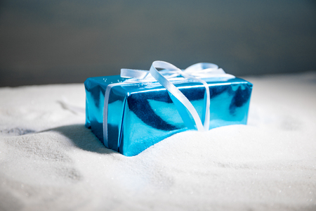 Christmas or New Year gift with ribbon in snow on bokeh background. Copy space for text. Winter card. Holiday and celebration concept.の写真素材