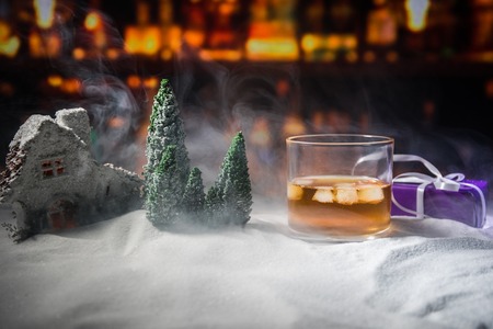 Glass with whiskey on snow with artwork Christmas decoration. Glass of whisky on white snow with a beautiful holiday background. Copy spaceの写真素材