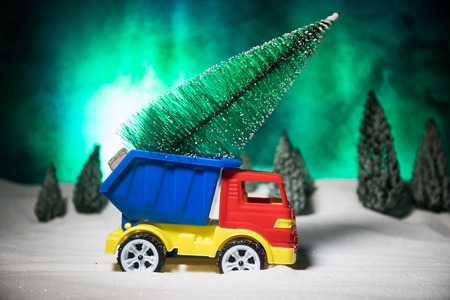 Christmas or New Year concept. Toy car carrying a Christmas tree through the forest in snowfall. Holiday decorated background. Selective focusの写真素材