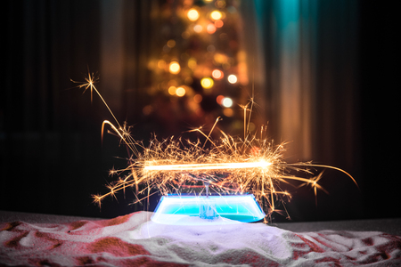 Glittering burning sparkler on snow with blurred Christmas tree on dark background. New Year Holiday concept with empty space for your text. Selective focusの写真素材